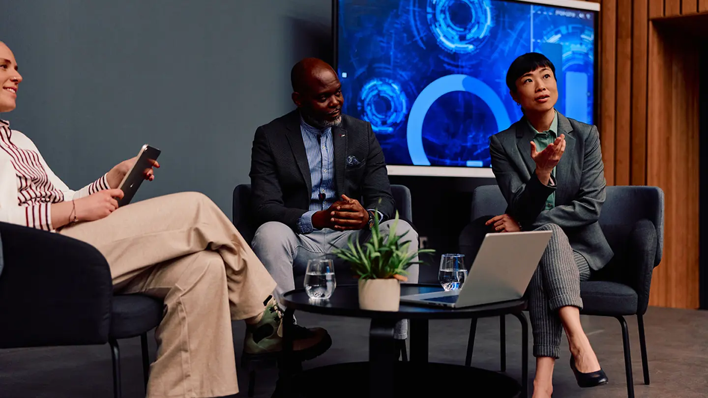 Business professionals in a panel discussion with a digital screen in a conference setting.