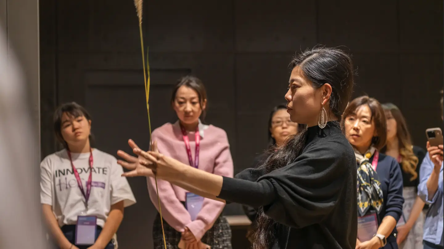 Woman demonstrating a traditional Japanese technique to an audience in a workshop setting.