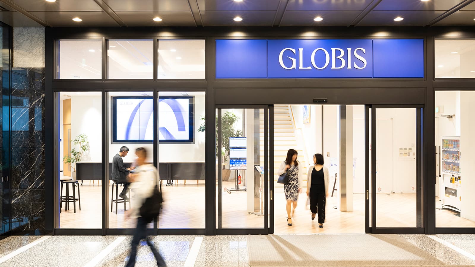 Entrance to the GLOBIS office with people walking in and out, including visible interior seating and a digital display