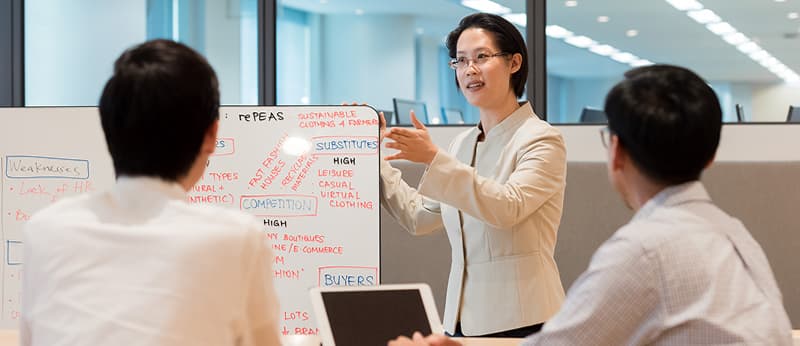 Instructor leading a corporate training session using a whiteboard, engaging with two professionals