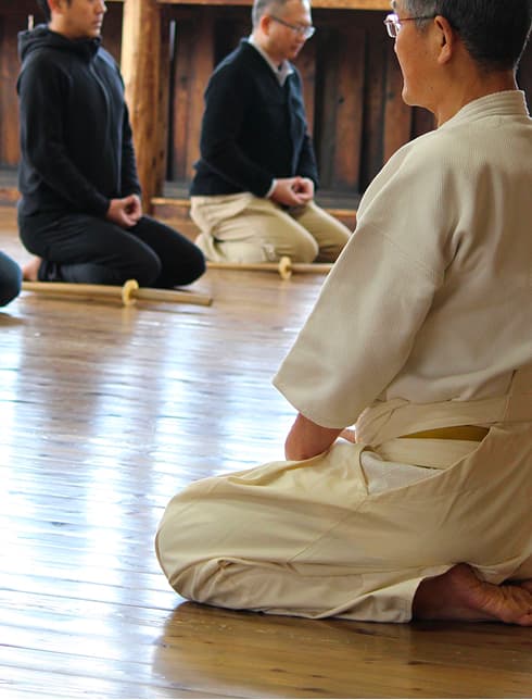 People kneeling on a wooden floor in a martial arts training session.