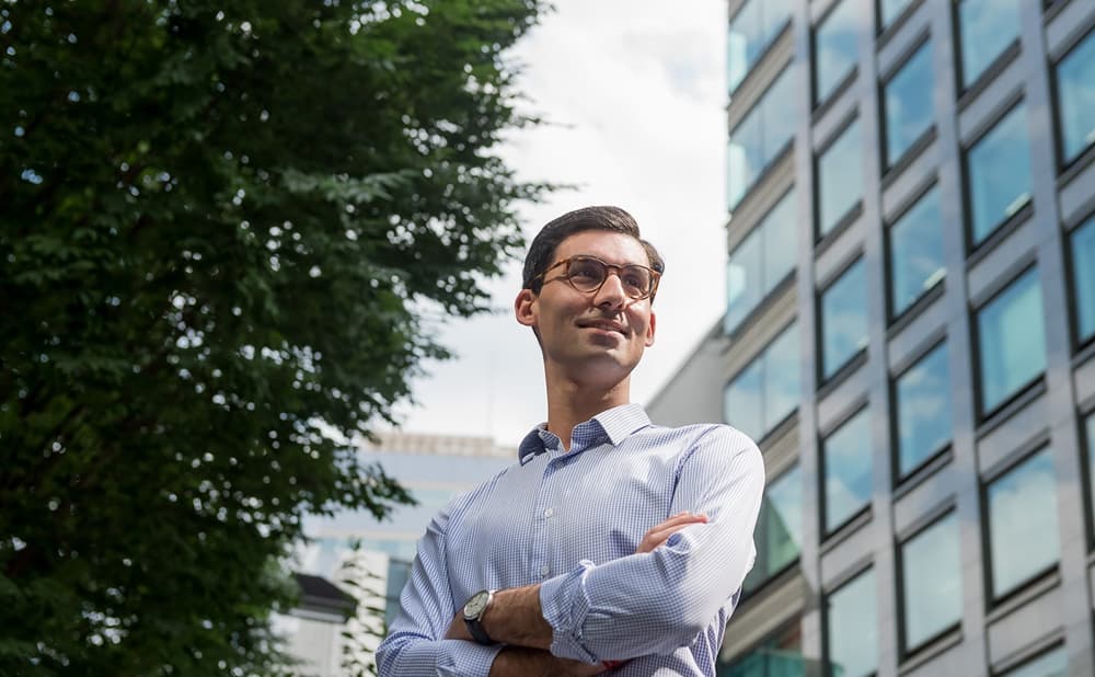 Confident young man standing outdoors with arms crossed, looking upward beside a modern office building