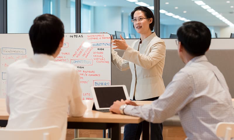 Instructor leading a corporate training session using a whiteboard, engaging with two professionals