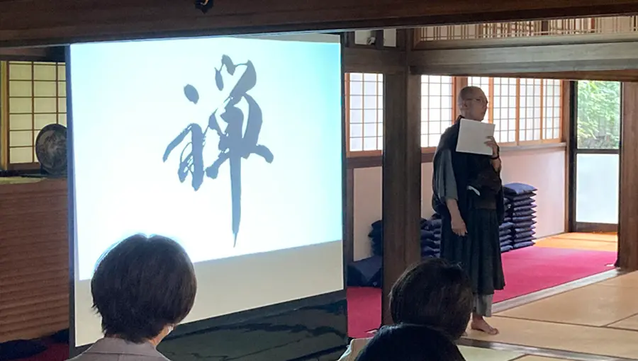 Person presenting in a traditional Japanese room with a screen displaying calligraphy.