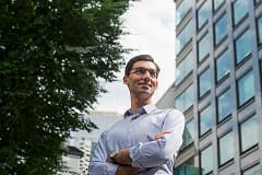 Confident young man standing outdoors with arms crossed, looking upward beside a modern office building