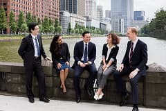 Five business professionals from diverse backgrounds sitting and conversing along a riverside in an urban cityscape