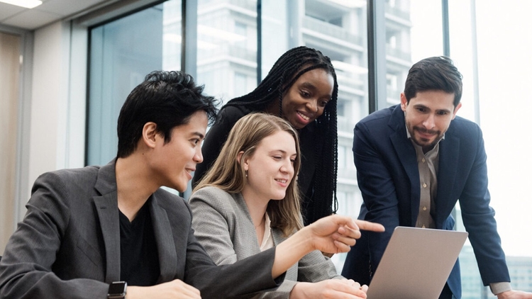 Four business professionals from diverse backgrounds collaborating and looking at a laptop PC