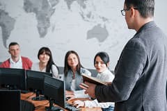 Business professionals attending a lecture while working on desktop computers in a meeting room