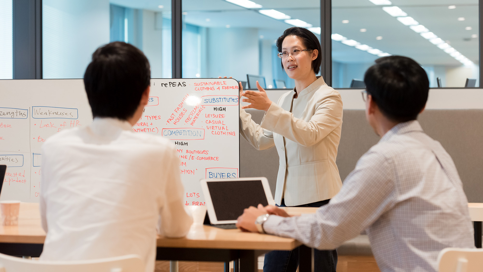 Instructor leading a corporate training session using a whiteboard, engaging with two professionals