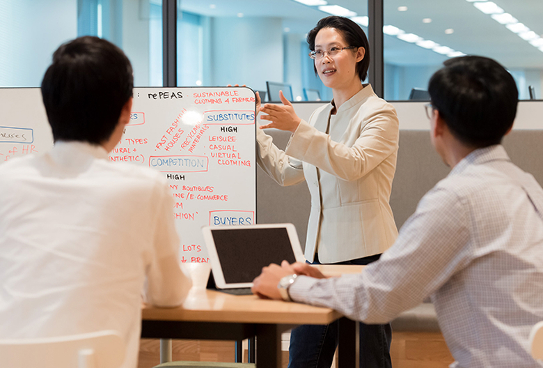 Instructor leading a corporate training session using a whiteboard, engaging with two professionals